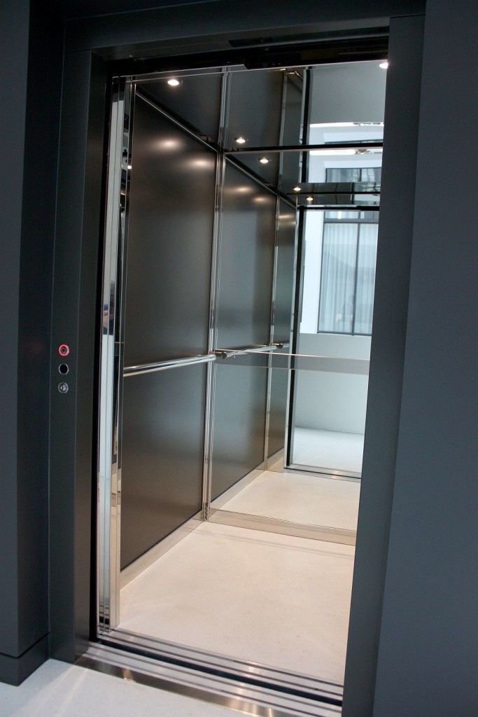 Close view of the lift cabin with a call button, stainless handrail and mirrored dark walls