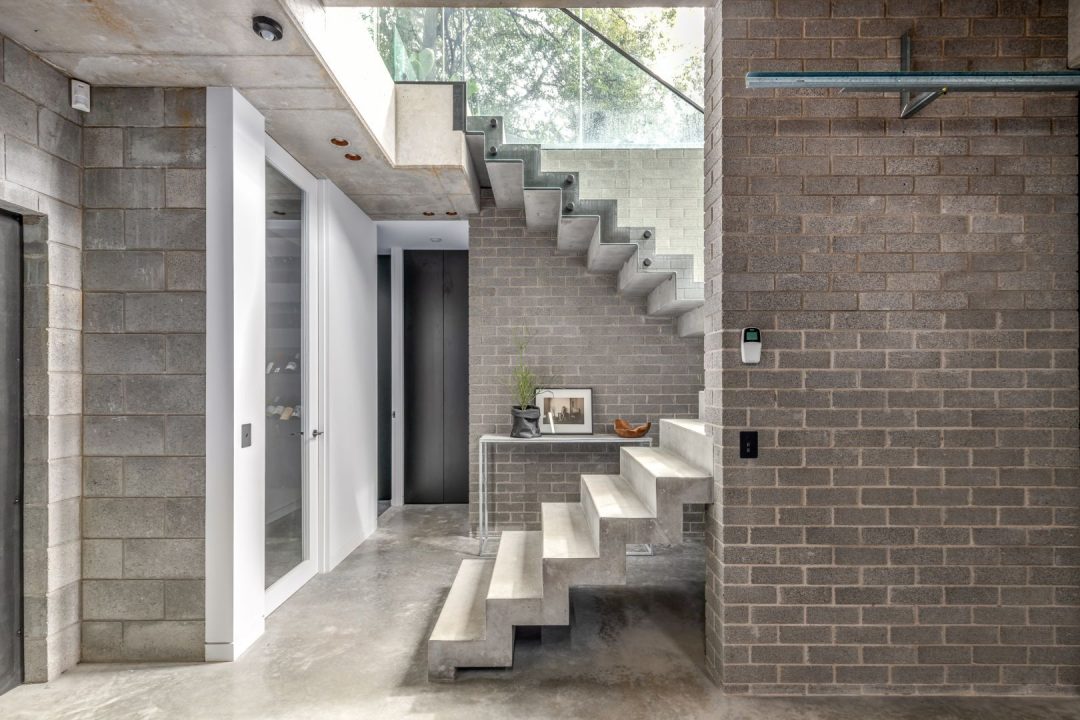 Concrete floating staircase beside a face-brick wall in a Merewether home