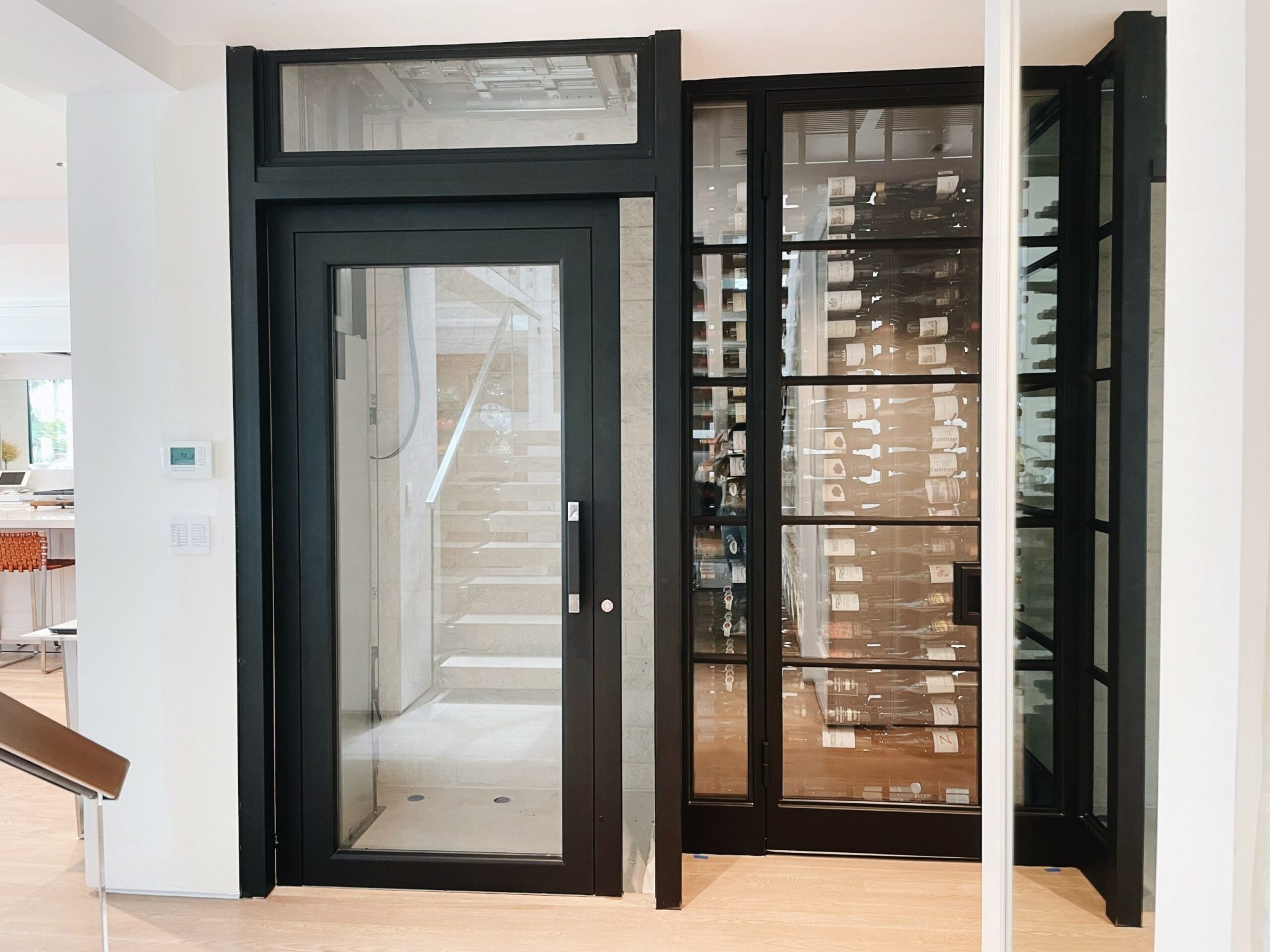 Black-framed E1 swing door lift with a glass door beside a glass wine display at a Newport Beach home