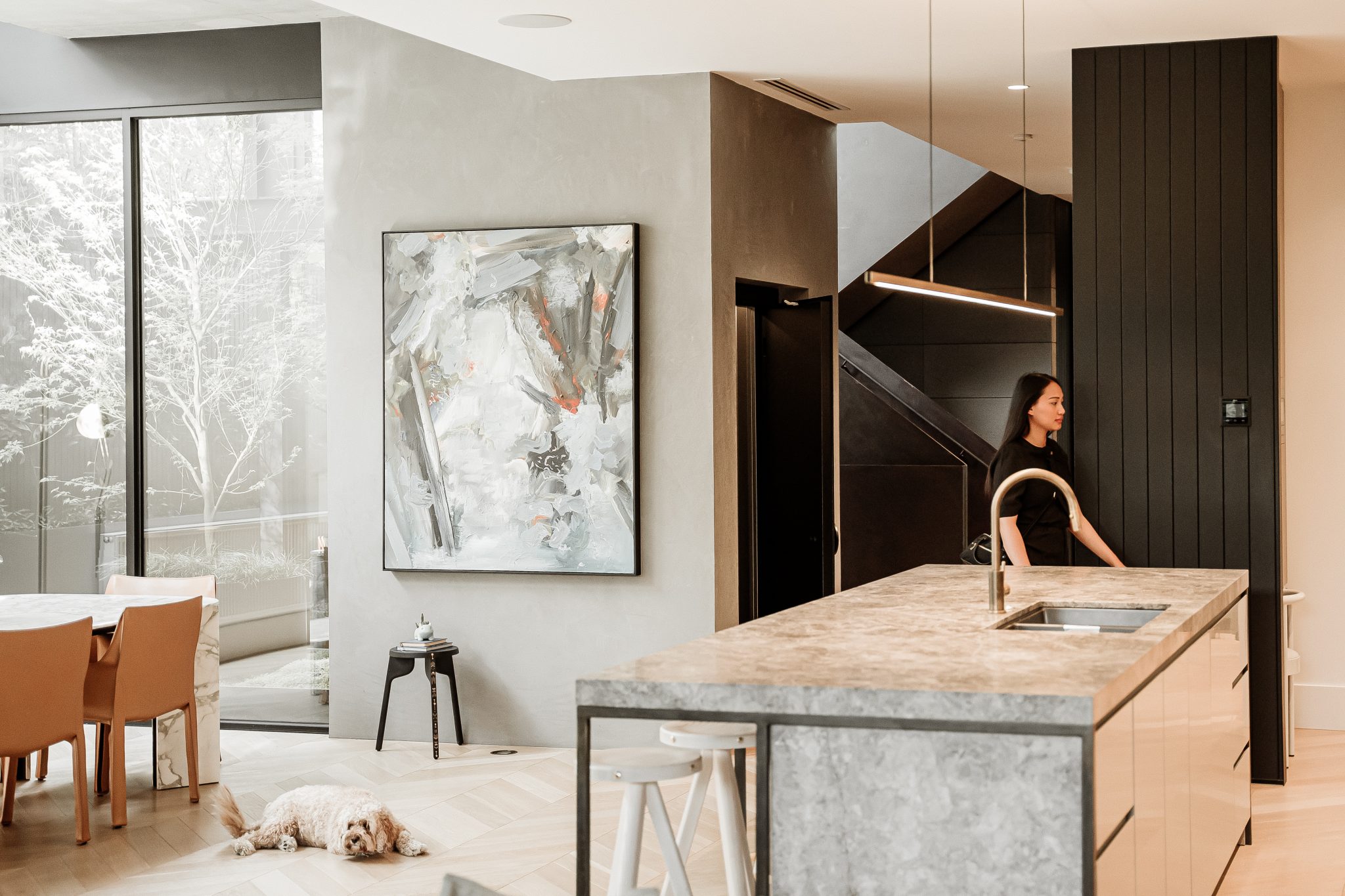 Open-plan Melbourne home with the E1 swing door lift beside the stairs, a woman at the kitchen island and the family dog on the floor