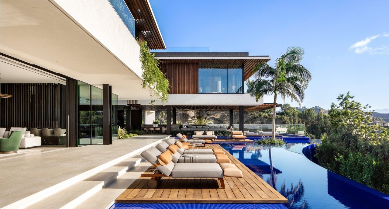 Poolside timber deck with sun loungers beside the infinity pool and the two storey Los Angeles estate