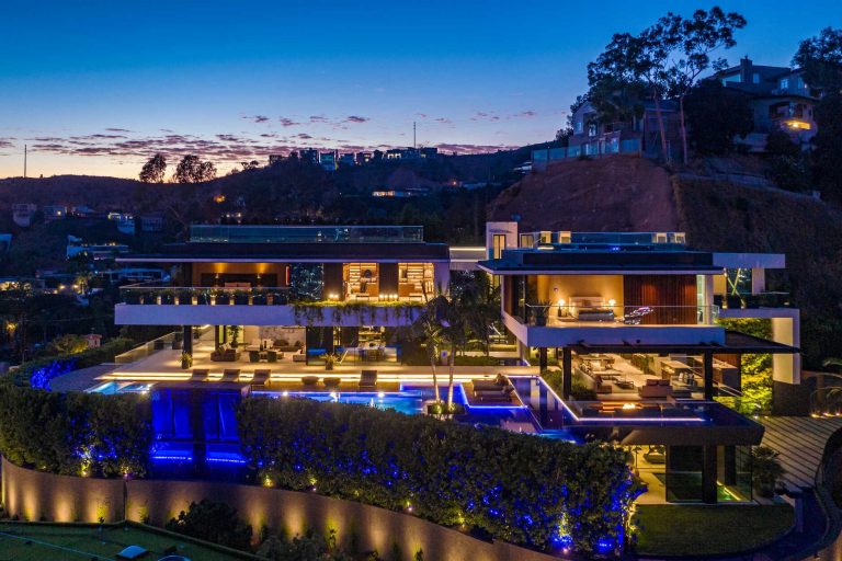 Hillside estate lit up at dusk with a blue lit pool and city lights beyond