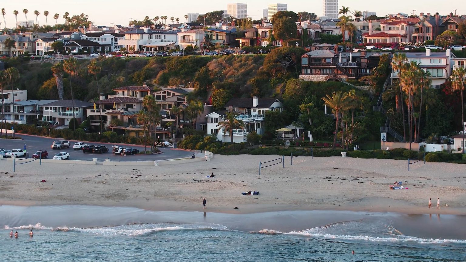 Corona Del Mar beach at sunset with coastal homes climbing the hillside above the sand