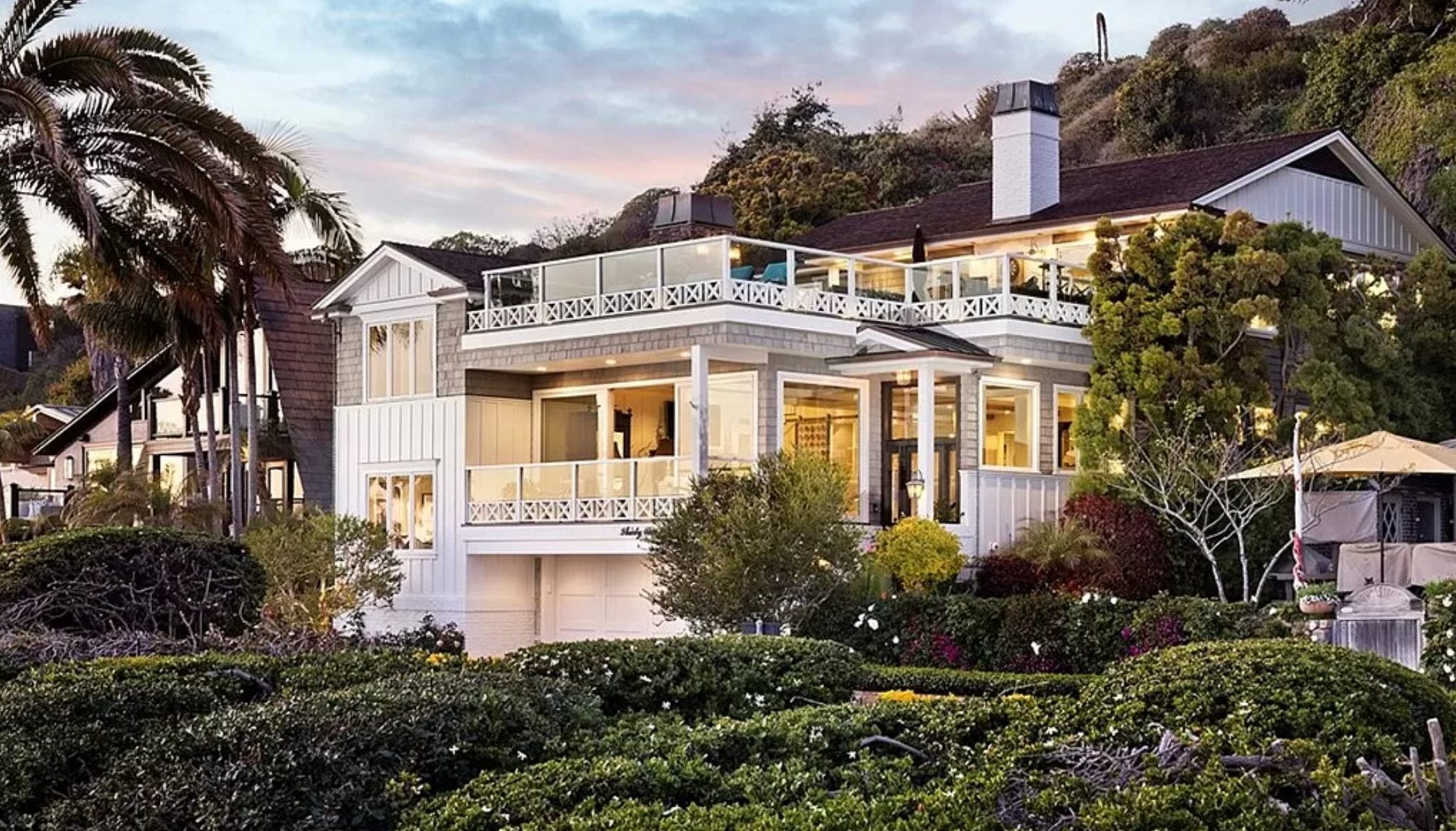 Oceanfront Corona Del Mar home with glass balustrades and a white shingle facade at dusk