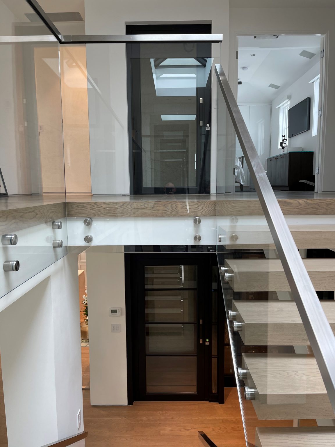 Black-framed E1 lift doors on two levels beside floating timber stairs with glass balustrade