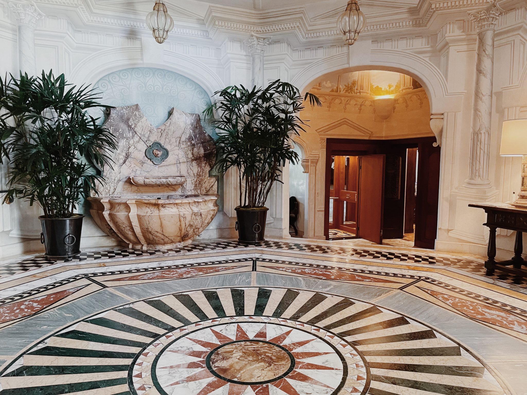 Grand entrance hall with a mosaic marble floor, potted palms and an arched doorway in the Malibu residence