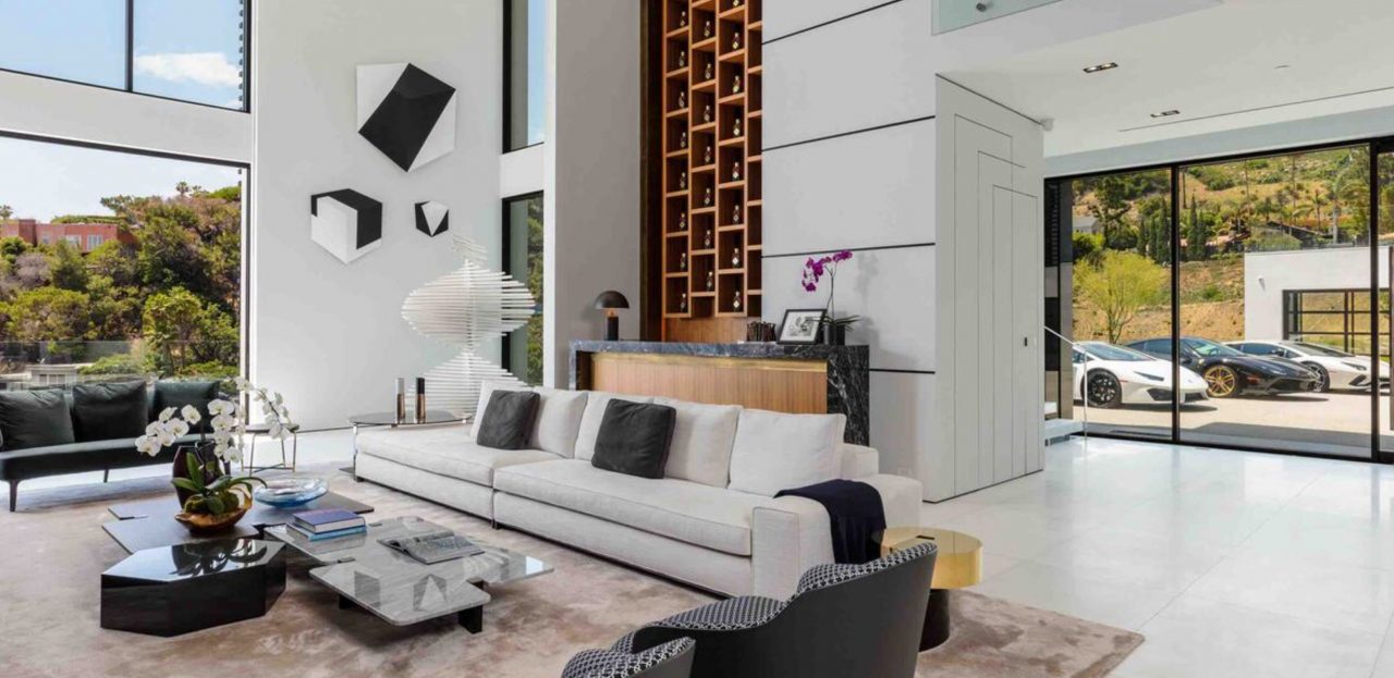 Double-height living room with a white sofa, a timber wine rack and glass doors to the driveway