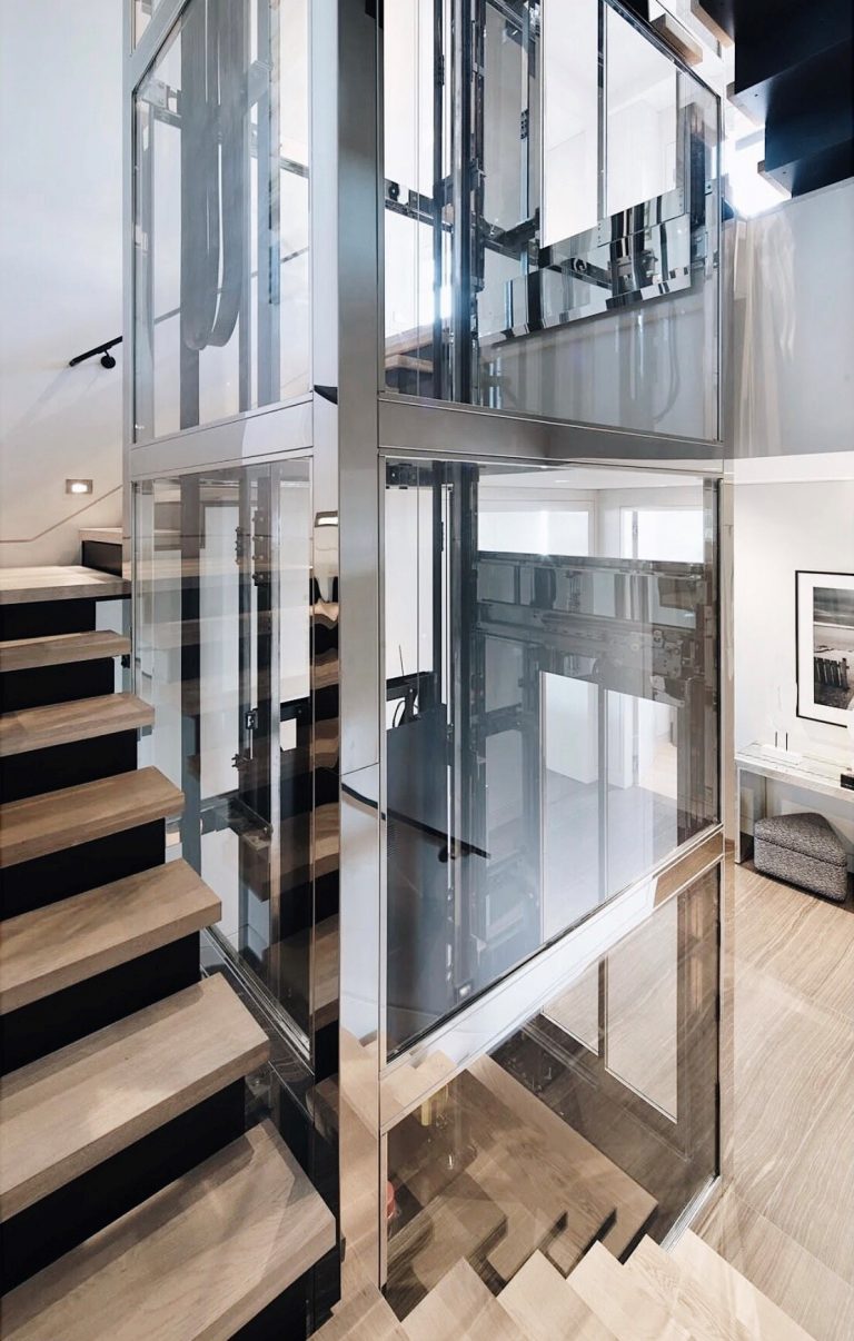 Glass lift with a polished stainless steel frame rising beside a timber staircase in a San Francisco home