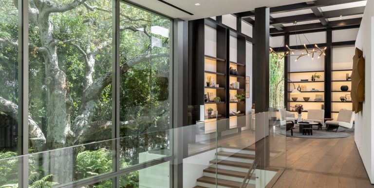 Living area with floor to ceiling glass walls, floating timber stairs and shelving in Los Angeles