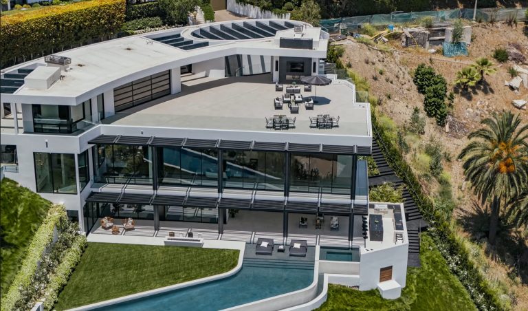 Aerial view of a large hillside home with glass walls and an infinity pool