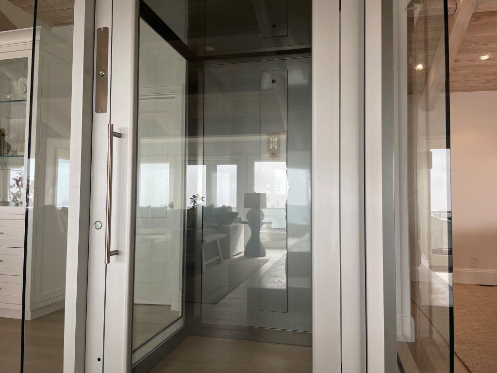 Close view of the glass lift door and brushed stainless steel frame reflecting the living room