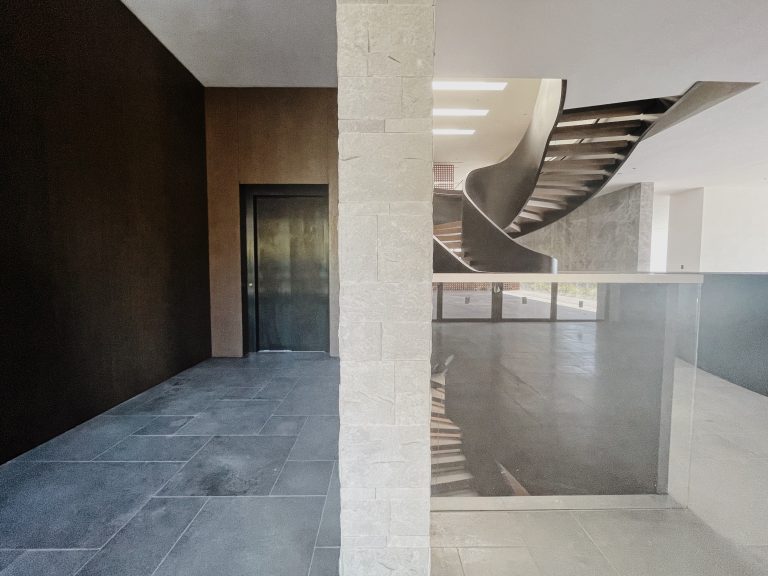 Slate tiled landing with a stone pillar, a curved staircase and a dark lift door
