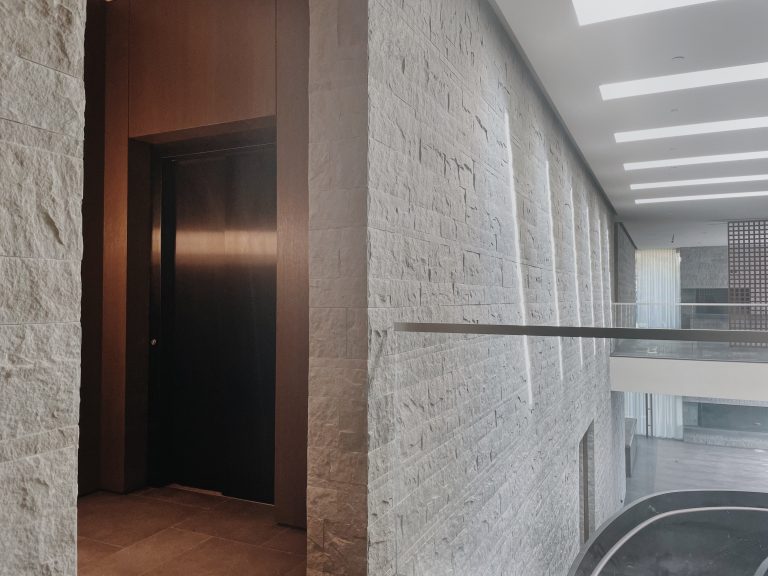 Dark lift door set in a timber wall beside a rough stone wall and a glass balustrade