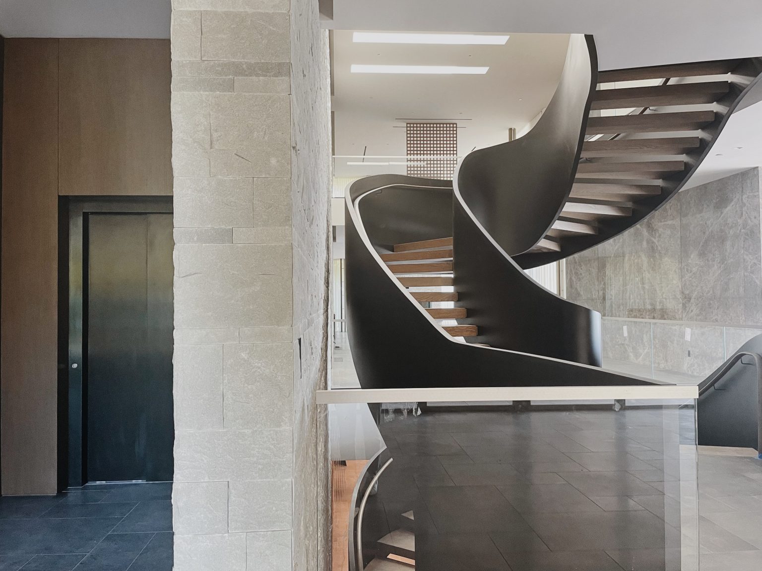 Curved sculptural staircase beside a stone feature wall and a dark lift door in a Los Angeles hillside home