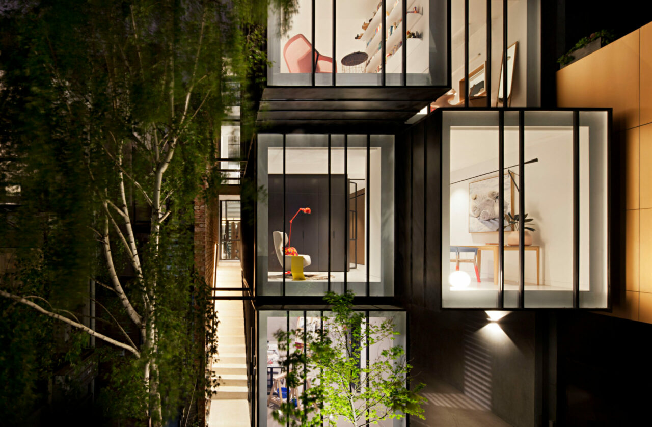 Illuminated windows of the multi-level home at night beside a leafy green wall