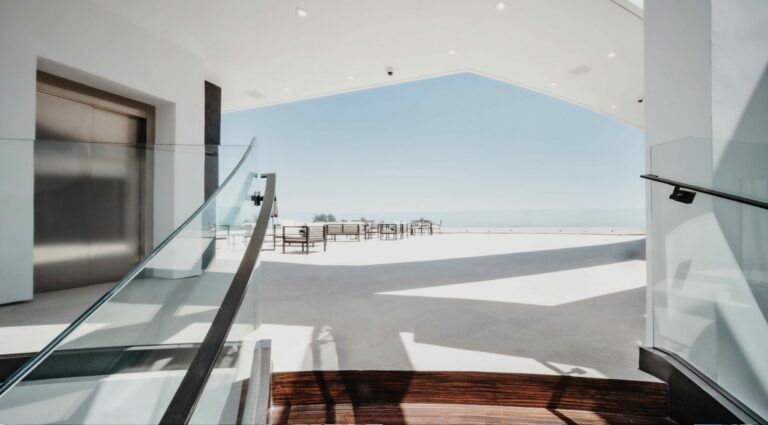 Brushed stainless steel lift door beside a glass balustrade, opening onto a terrace with a sea view