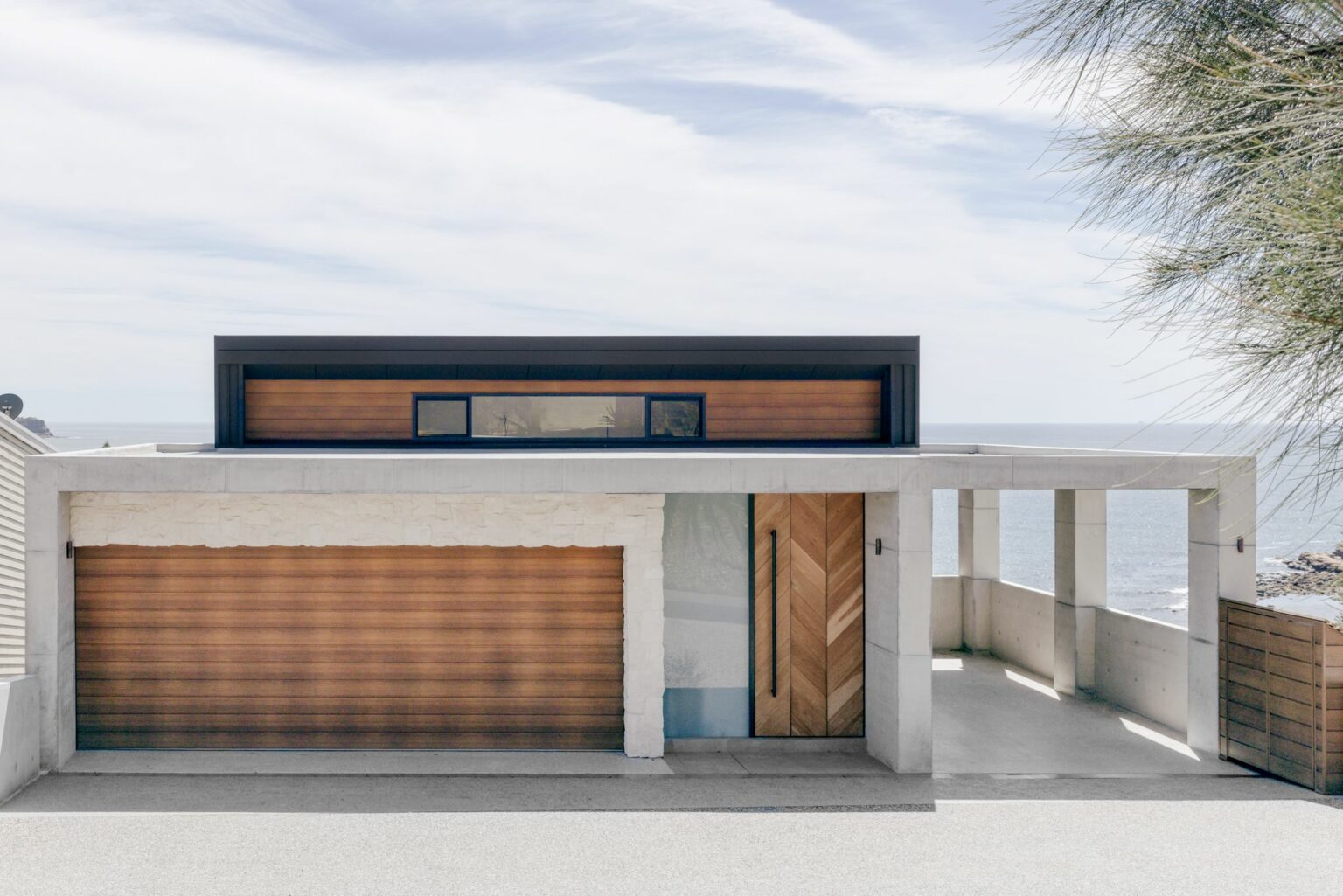 Street front of the Avoca Beach home with a timber garage door, limestone and concrete, and the ocean behind