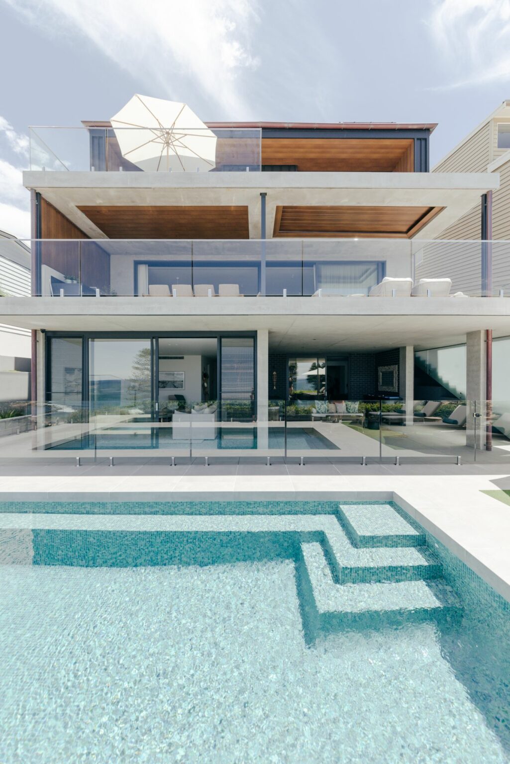 Rear of the three-level Avoca Beach home with glass balustrades above the tiled pool