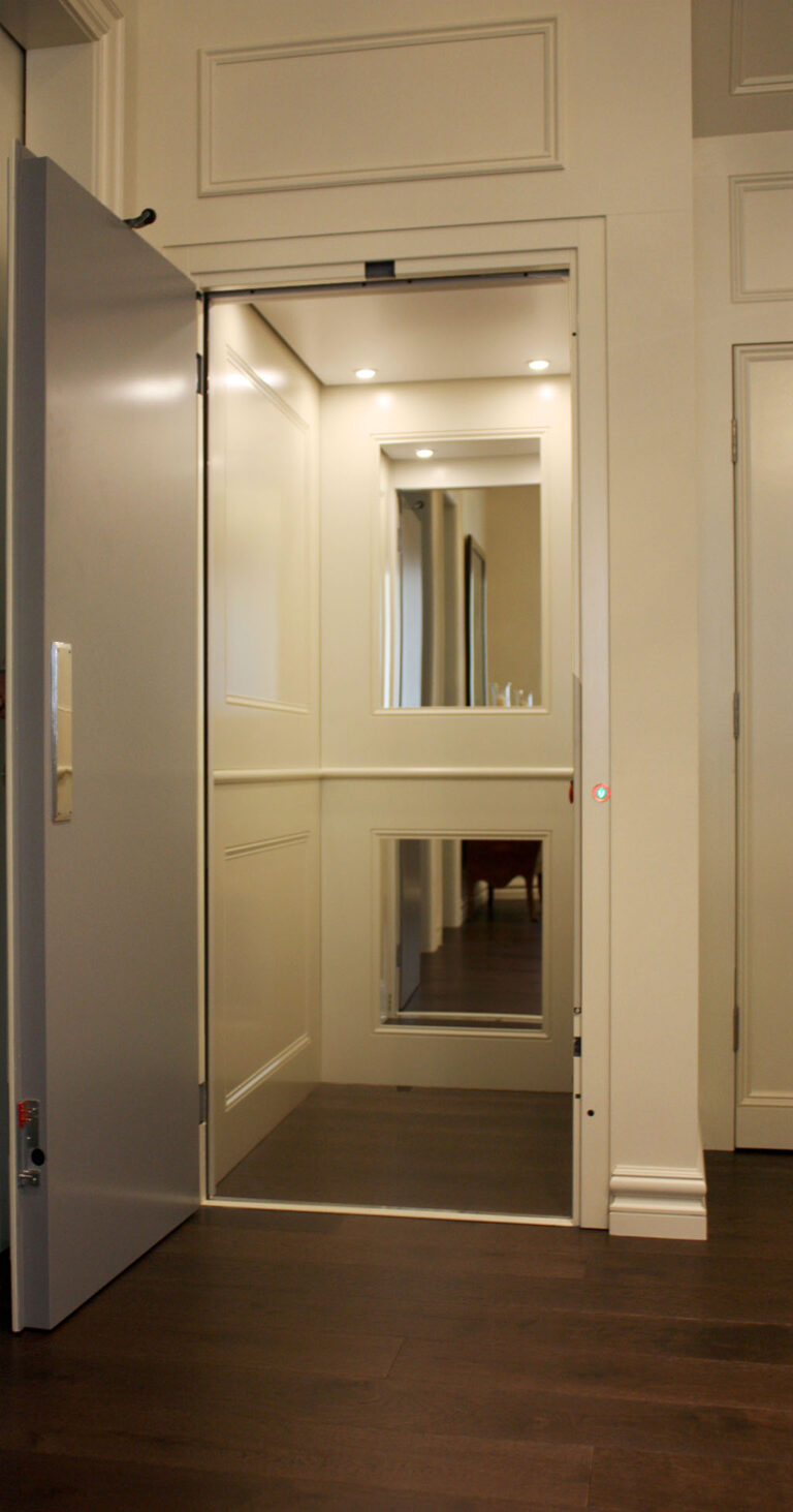 Open E1 lift door with a white panelled interior and a mirror, seen from the hallway
