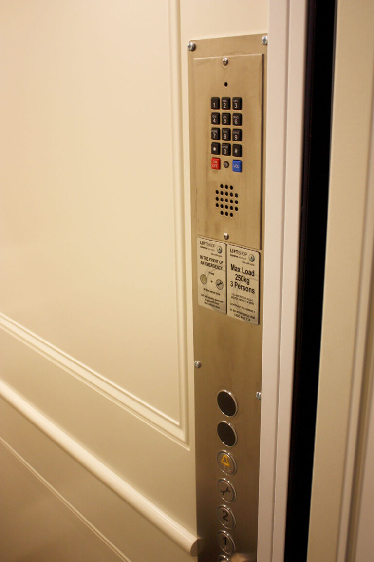 Brushed stainless steel lift button panel with a keypad and floor buttons beside a white panelled wall