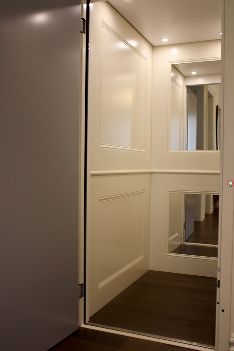 Inside the white panelled E1 lift car in Tamarama, with a mirror and the grey swing door open