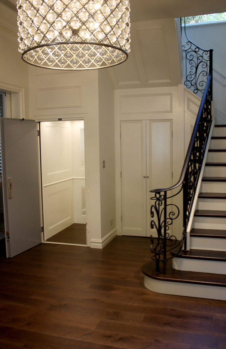 Hallway in Tamarama with a chandelier, a staircase and the open lift door on the left