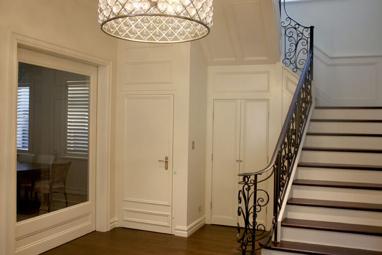 Entry hall with a crystal chandelier, wrought iron stair rail and white panelled walls in Tamarama