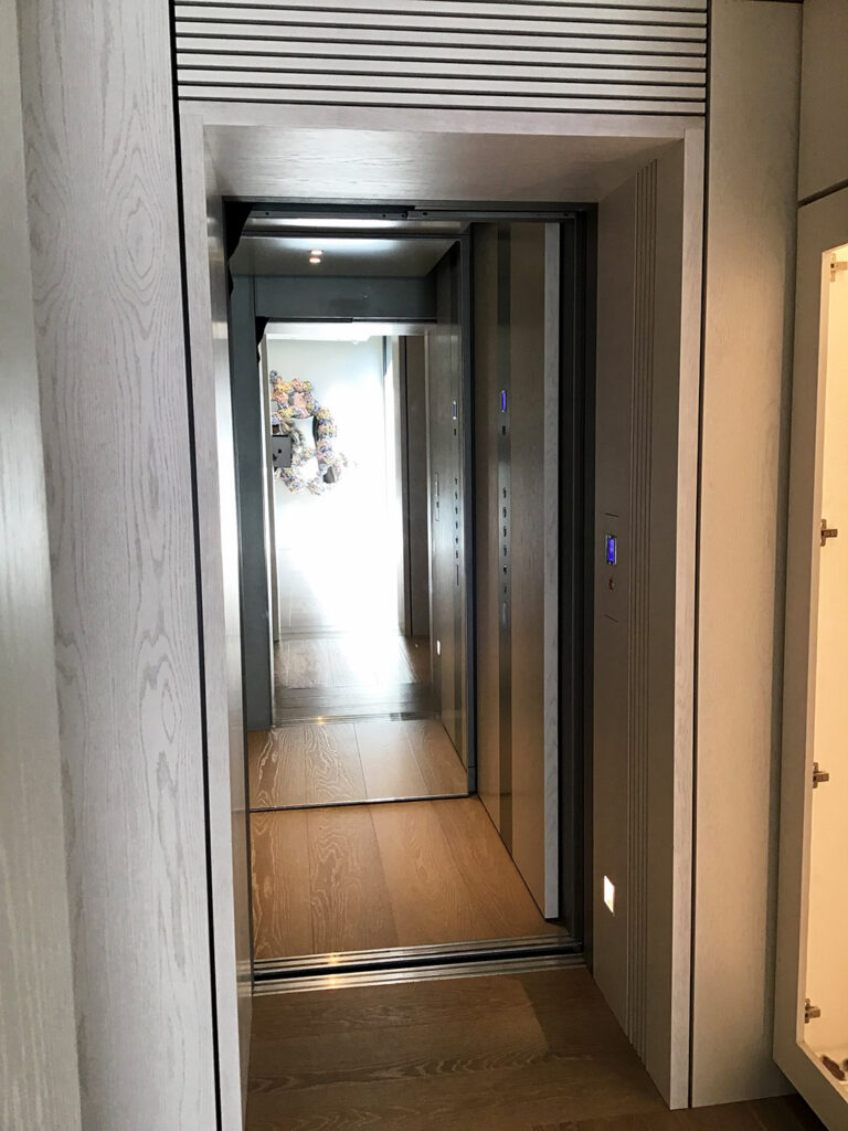 E2 lift doors opening onto a long hallway with a timber floor and a wood textured wall