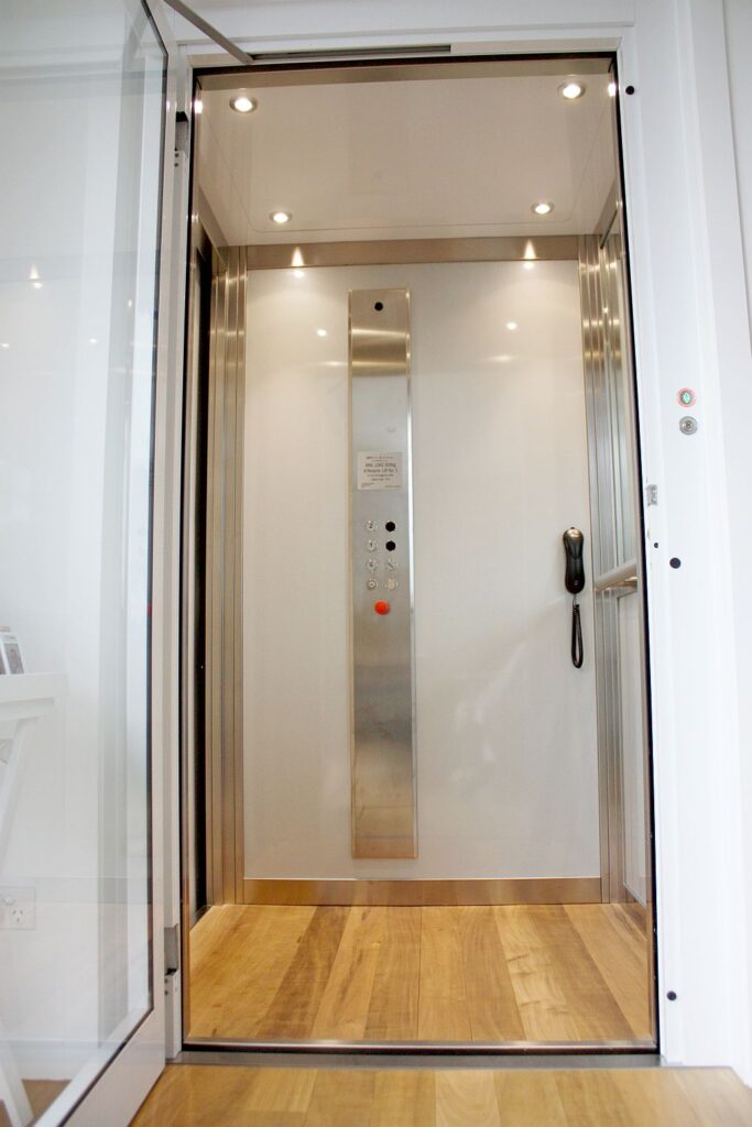 Inside the lift cabin: light grey walls, a brushed stainless steel control panel and a timber floor