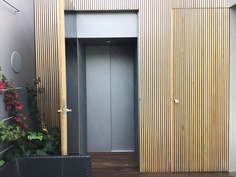 Lift door beside timber batten wall panels and a flowering plant in Vaucluse