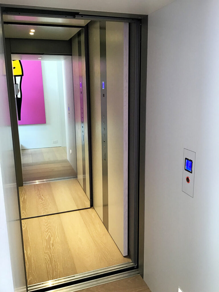 Inside the E2 lift car with a control panel and a bright pink artwork down the hall