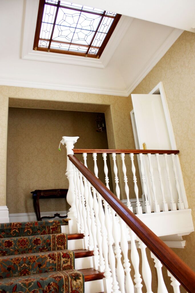 Staircase with a white balustrade, timber handrail and a stained glass skylight above in the heritage home