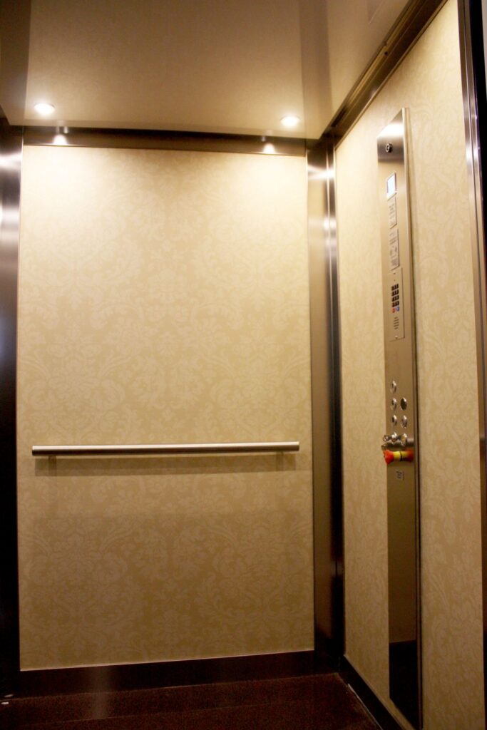 Inside the lift cabin with patterned wallpaper walls, a stainless steel handrail and ceiling downlights