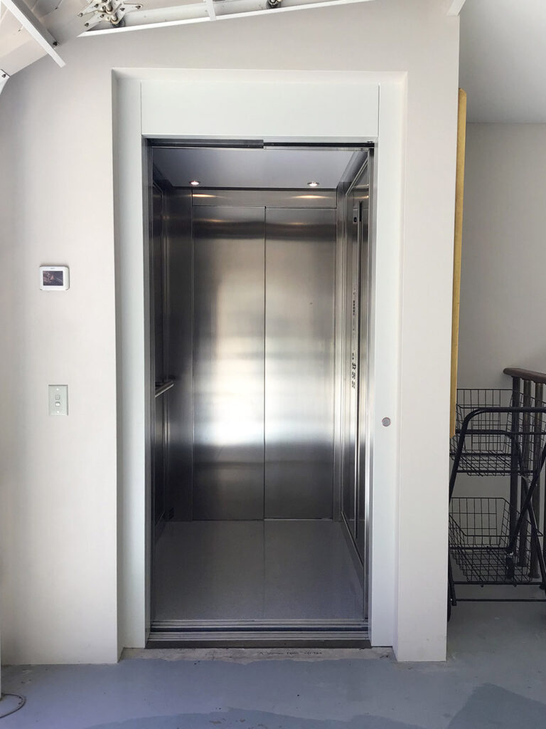 Stainless steel lift doors set in a cream wall beside a shopping trolley