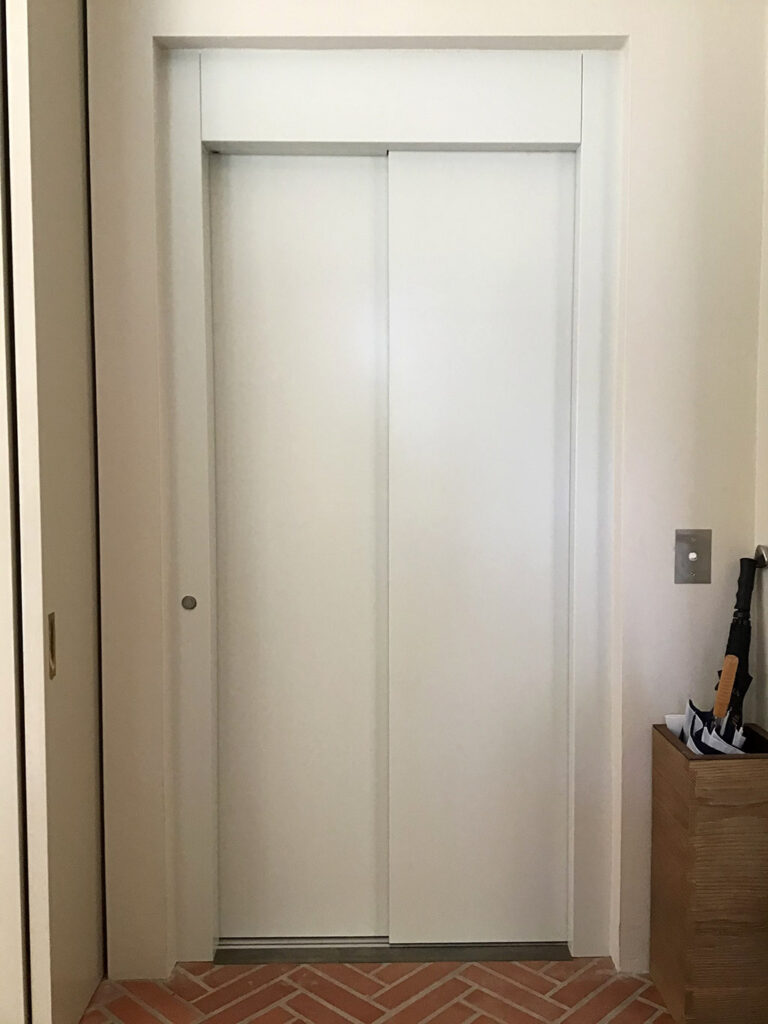 White sliding lift doors in a cream wall above a herringbone brick floor, Mosman
