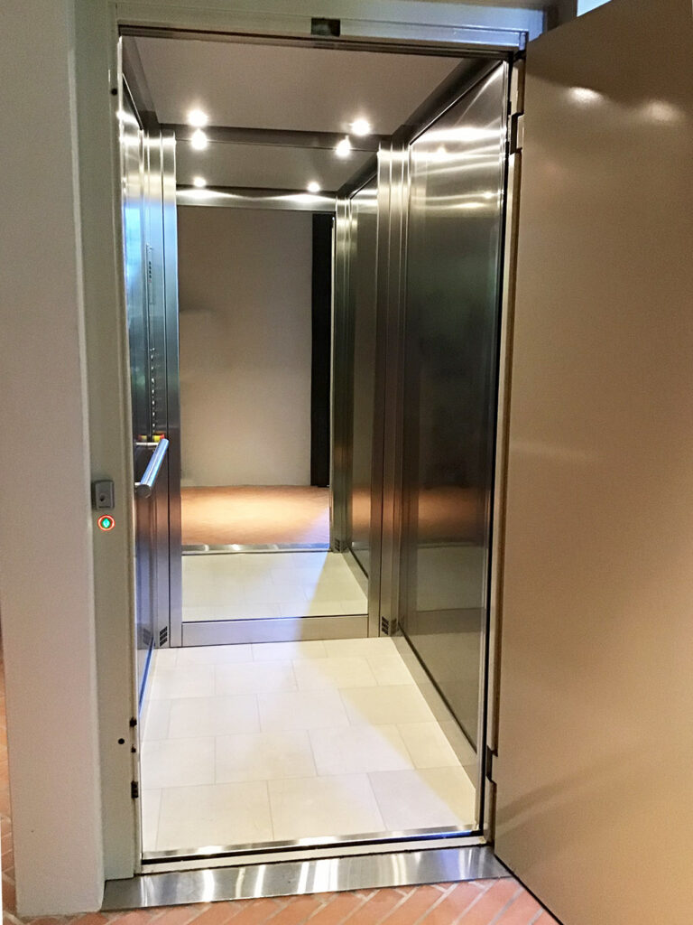 Open lift door showing a stainless steel cabin with downlights on a herringbone brick floor, Mosman