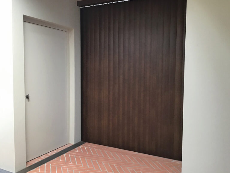 Closed white lift door beside a dark timber panel on a brick-paved landing
