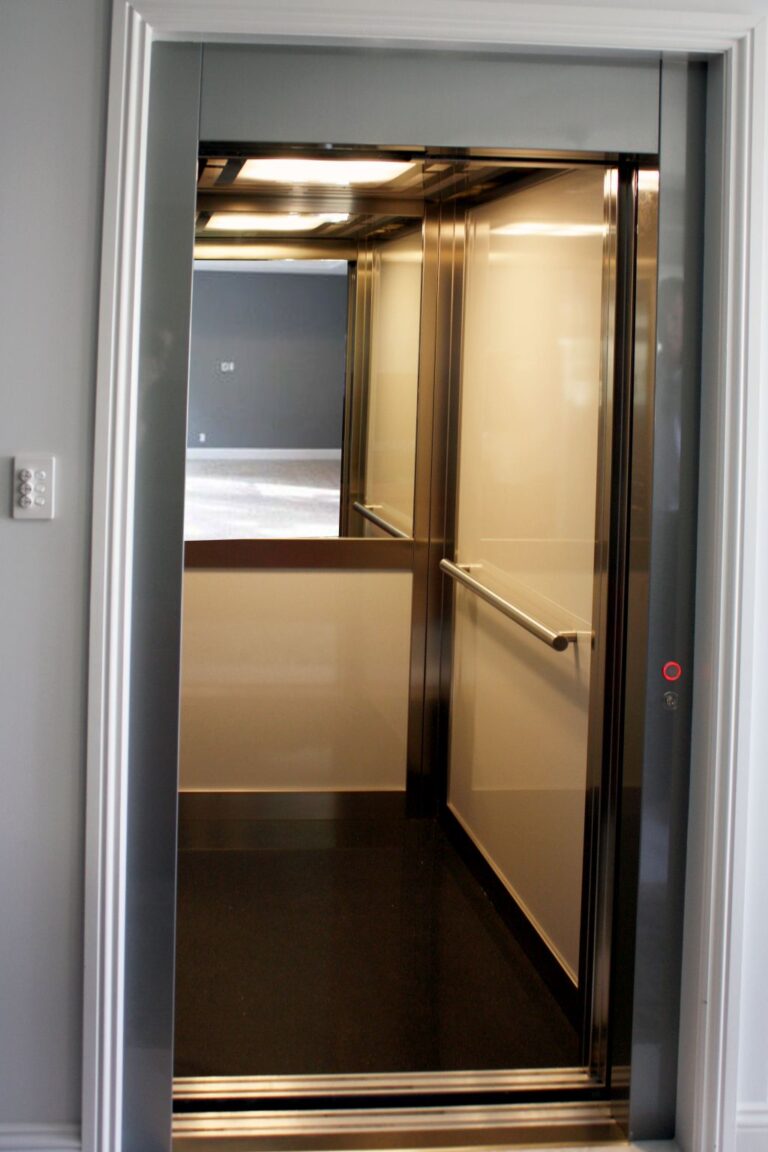 Inside the lift cabin, with a half mirror on the rear wall, a stainless steel handrail, Grigio panels and a dark floor