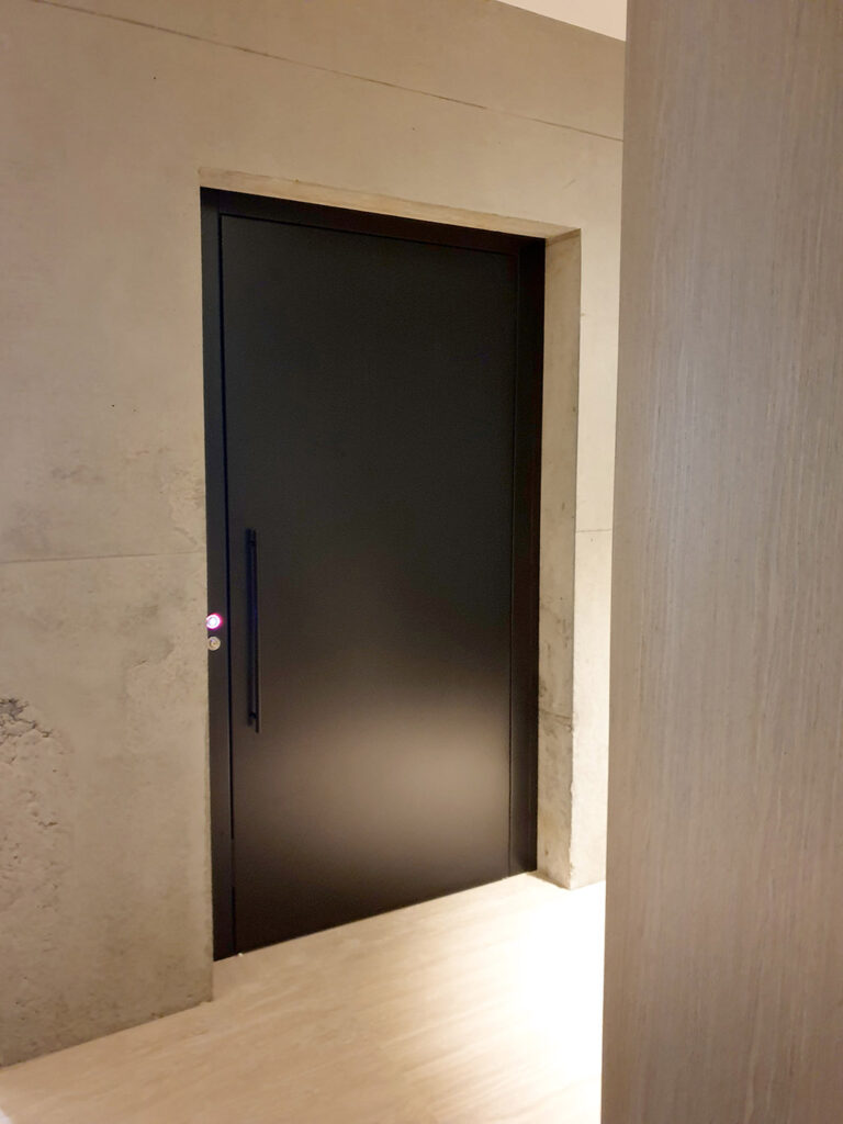 Closed traffic black lift door with a bar handle in a concrete and timber wall, Toorak