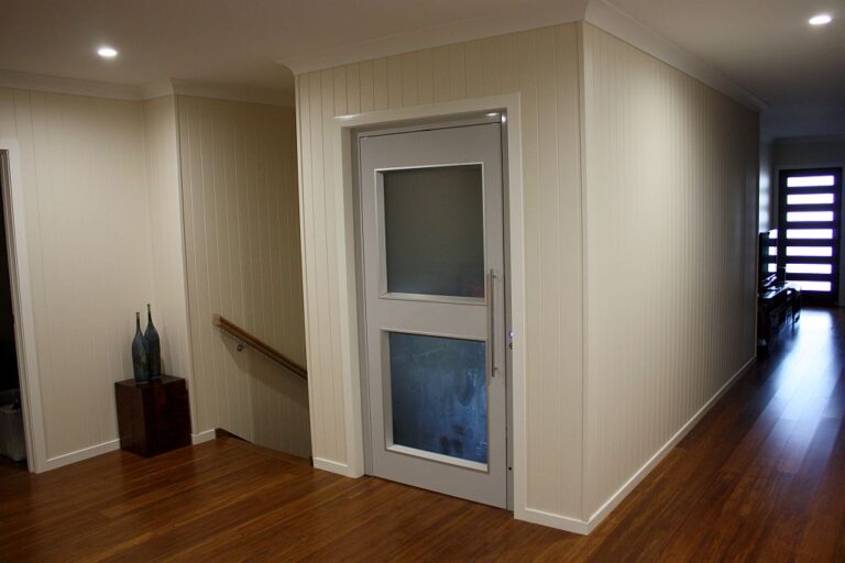 Upper hallway with a timber floor, white panelled walls and the lift's etched glass door