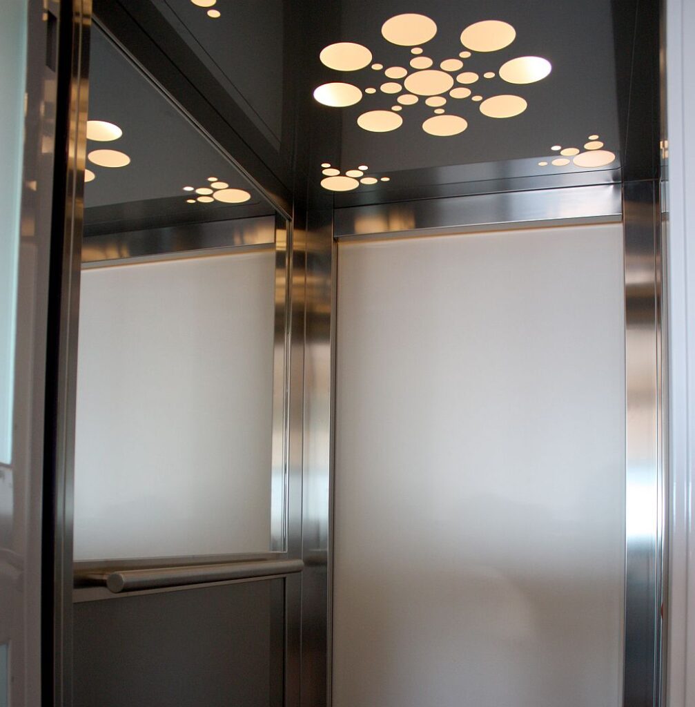 Lift cabin interior with etched glass panels, stainless steel profiles and circular ceiling lights