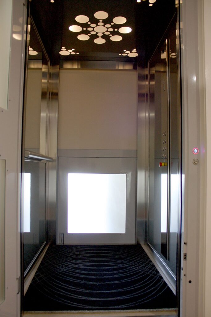 Straight-on view into the three-level ElfoLift cabin with a circular pattern ceiling light, stainless steel trim and a dark patterned floor