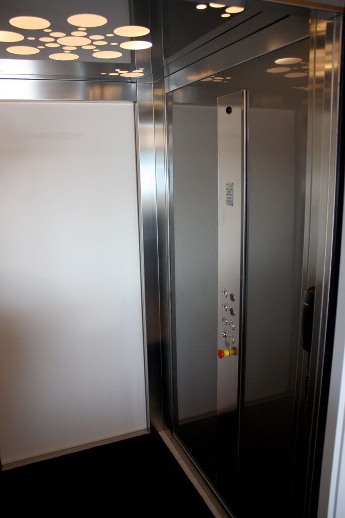 Corner of the lift cabin with stainless steel panels and a control panel beside the door
