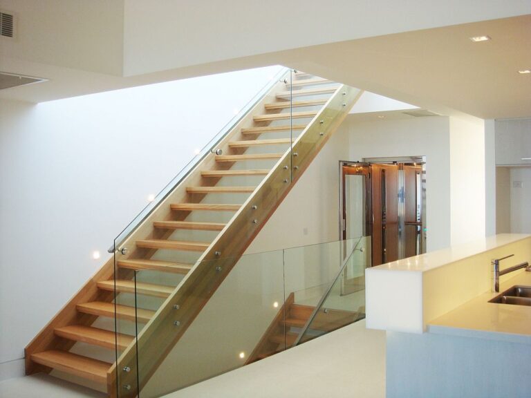 Timber stair with a glass balustrade and a lift visible near the kitchen in a Port Melbourne home