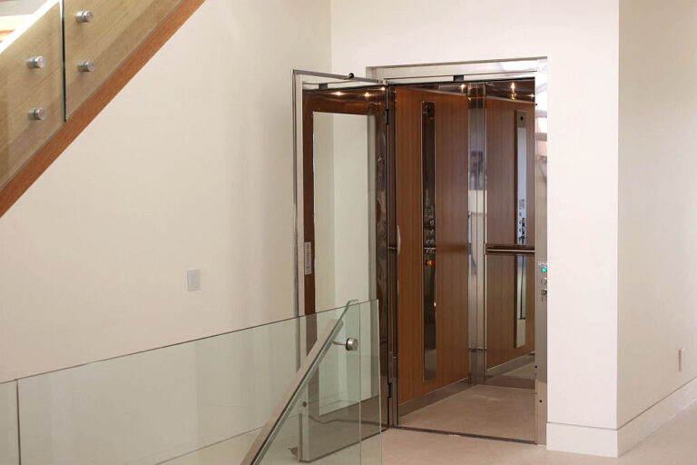 Timber panelled lift doors open beside a glass balustrade and stair