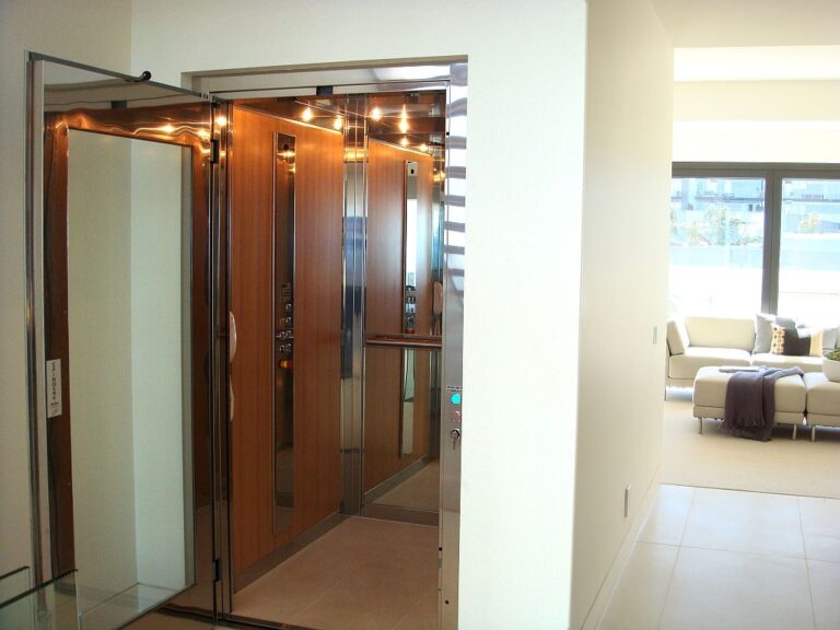Open home lift with timber wall panels and downlights facing a living room with a sofa
