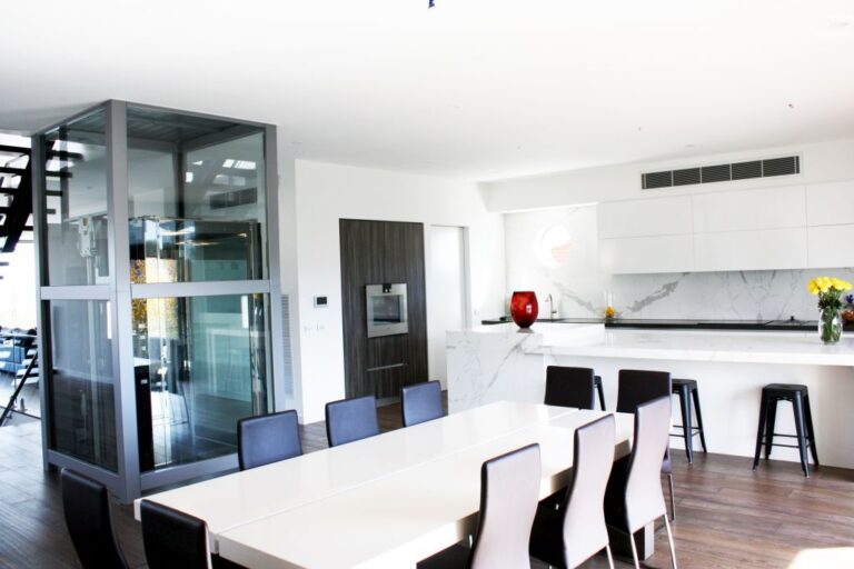 Glass lift shaft in an open plan kitchen and dining area with white benchtops