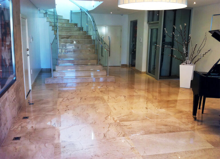 Polished stone floored hall with a wide staircase, a grand piano and the glass lift beyond