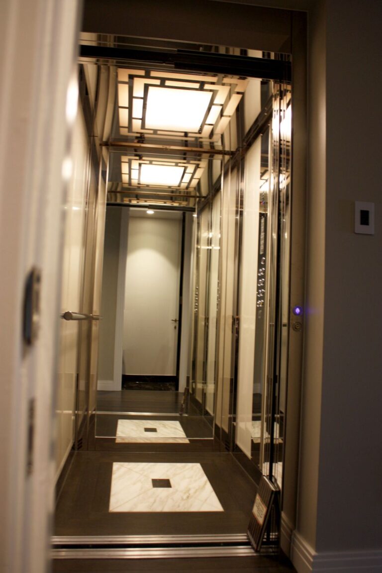 Long view through the duplex lift cabin, with glass walls, a marble floor inlay and a light panel overhead