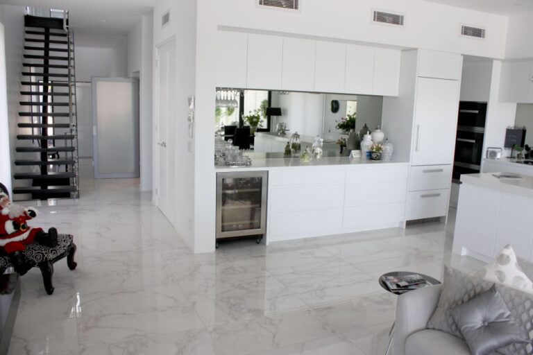 Open-plan kitchen with a white marble floor and a black staircase near the lift landing door in the Red Hill home